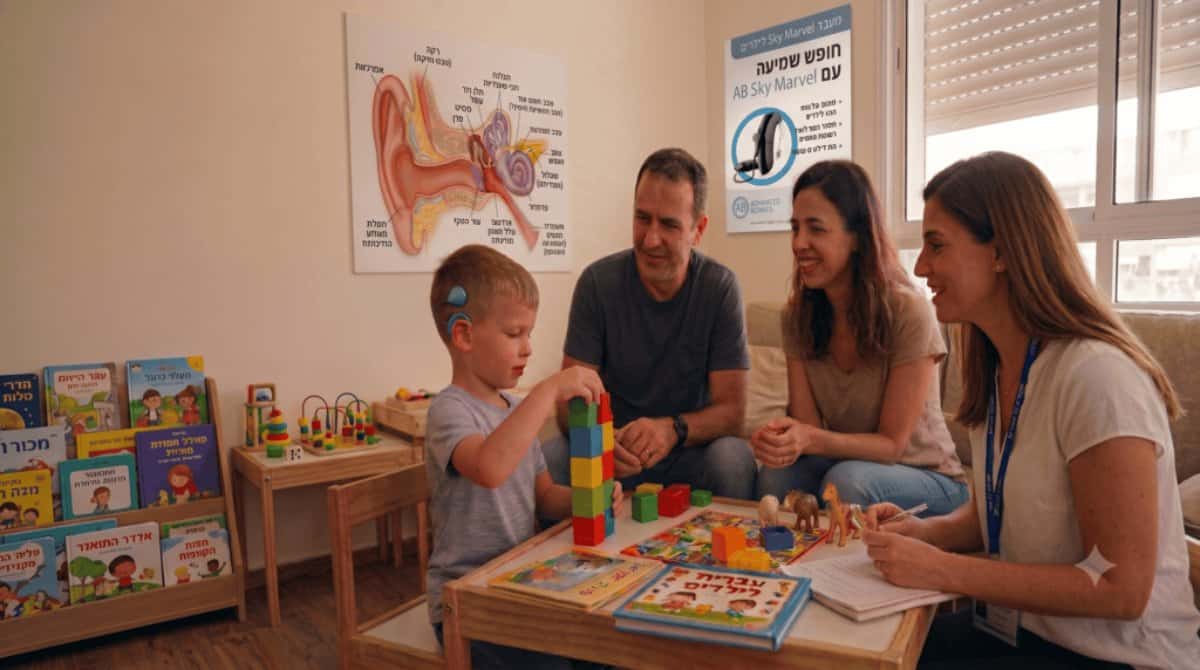 ילד עם שתל שבלול משחק לצד משפחתו ואשת מקצוע